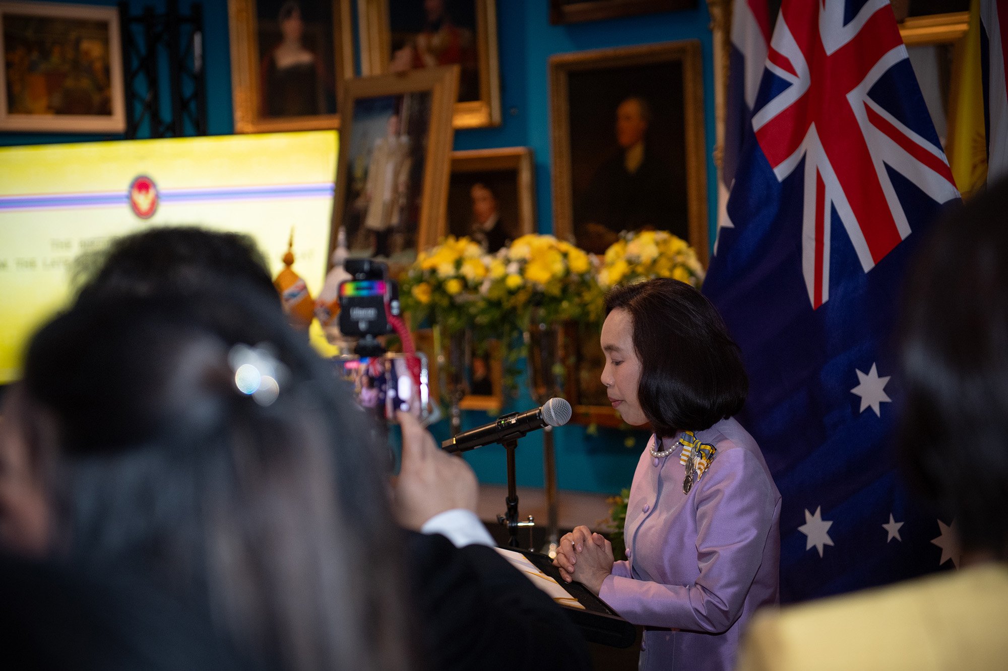 The Thai Consulate General gives a speech at the National Thai Day event surrounded by a crowd and the Australian flag in Sydney in 2023.